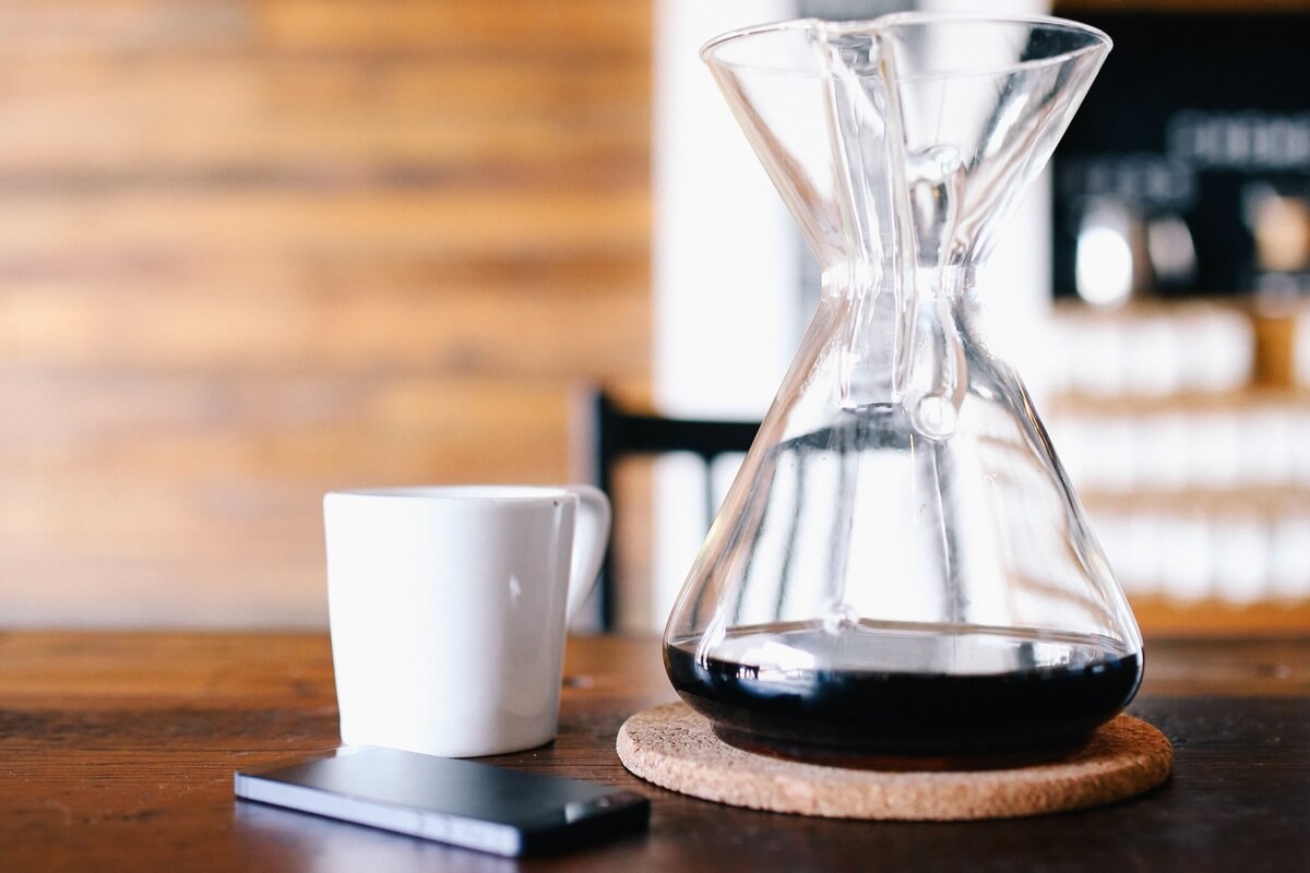 Aufnahme eines Kaffeebechers und einer gläsernen Kaffeekanne auf einem Holztisch