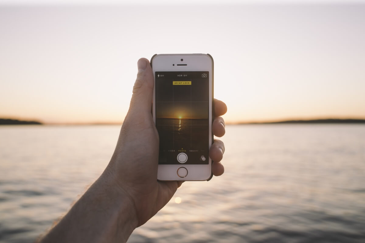 Eine Hand hält ein Smartphone, das den Sonnenuntergang fotografiert